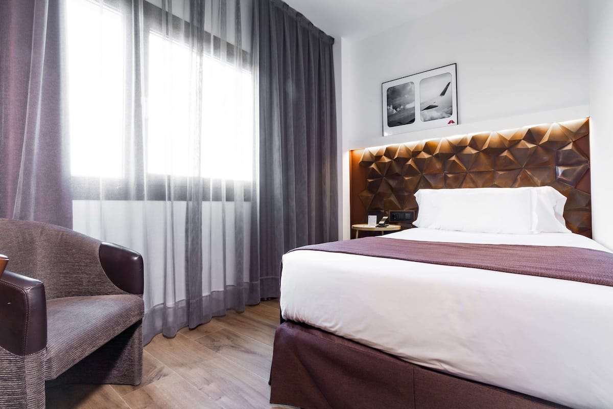Ein Hotelzimmer mit einem großen Bett, einem Sessel, einem Nachttisch und einem Wandbild.