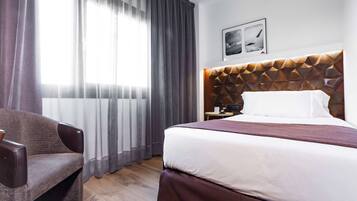 Ein Hotelzimmer mit einem großen Bett, einem Sessel, einem Nachttisch und einem Wandbild.