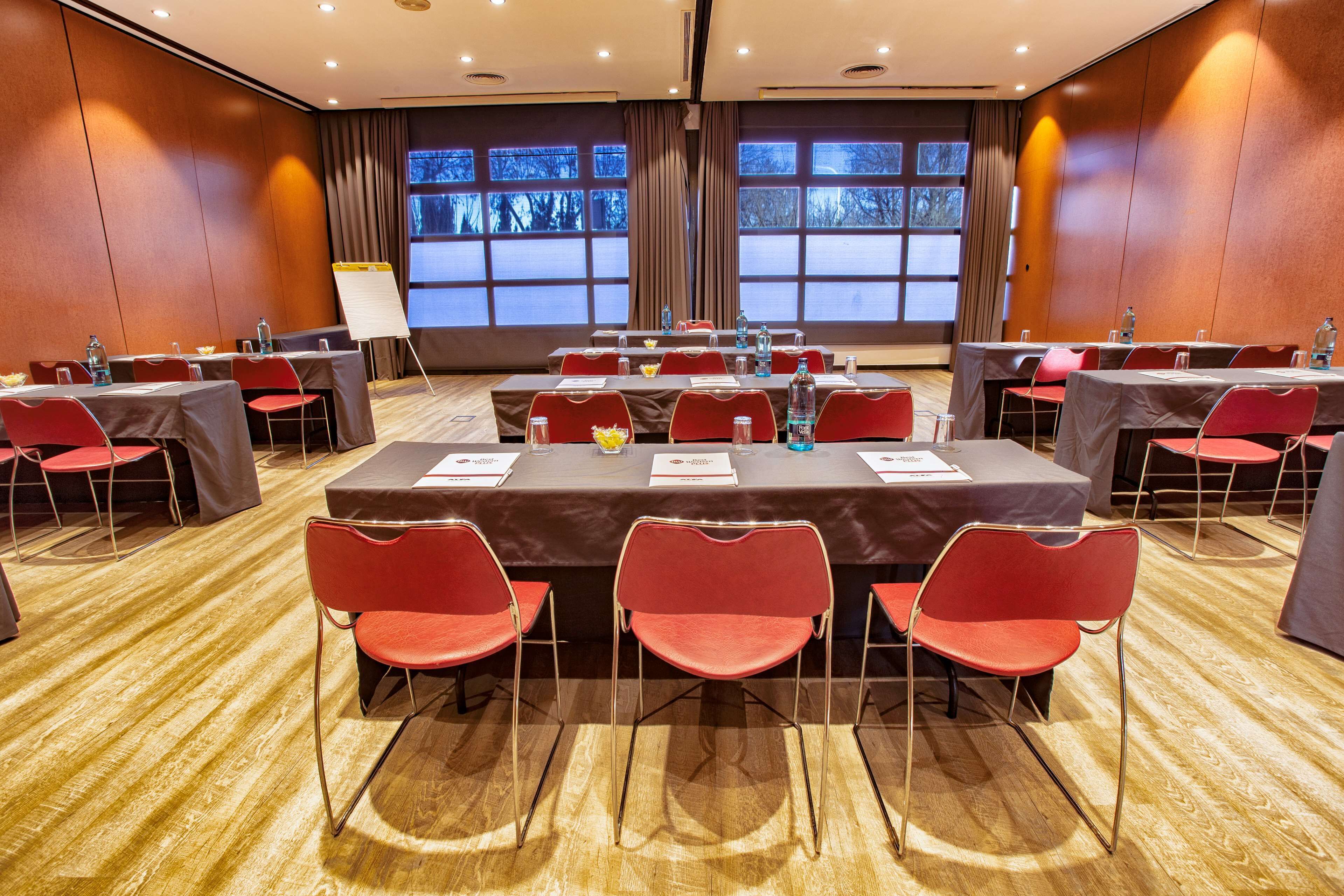 A conference room with multiple tables and red chairs, large windows with curtains, and a whiteboard.