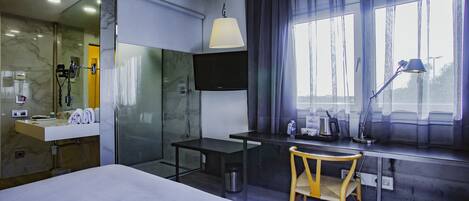 Une chambre d’hôtel moderne équipée d’un lit, d’un bureau, d’une chaise, d’une télévision et d’une fenêtre avec des rideaux.