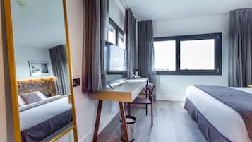 Une chambre d’hôtel avec un lit, un bureau, une chaise, une grande fenêtre et un miroir.