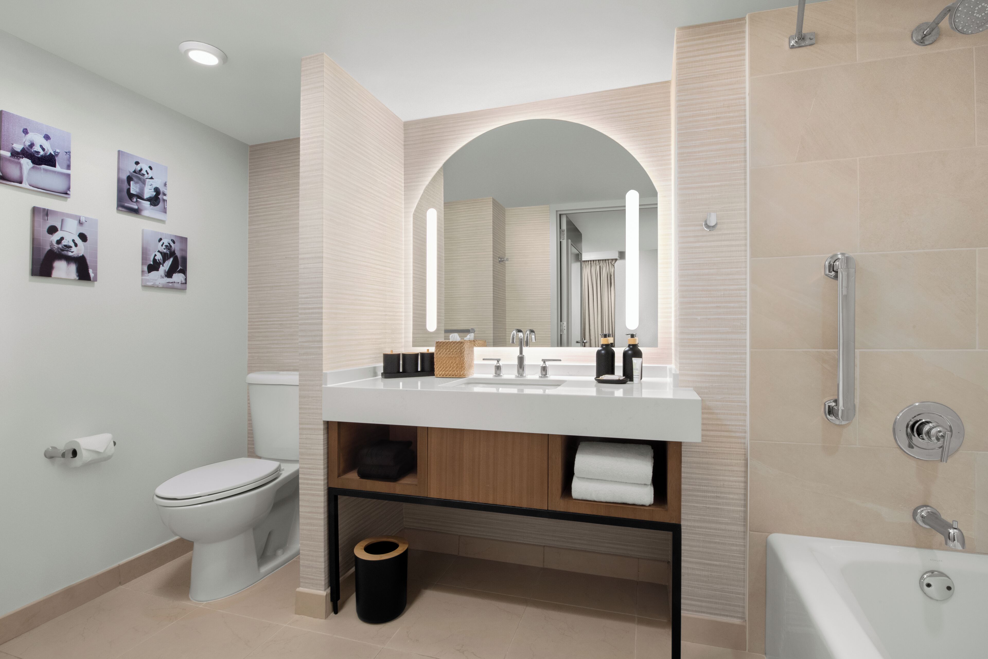 A modern bathroom with a toilet, sink, and shower. There are panda-themed wall art and a mirror above the sink.