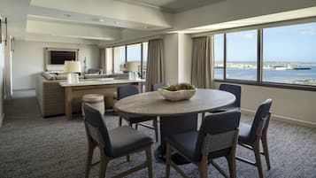 A modern hotel room with a dining area, a sofa, a TV, and a view of the sea.