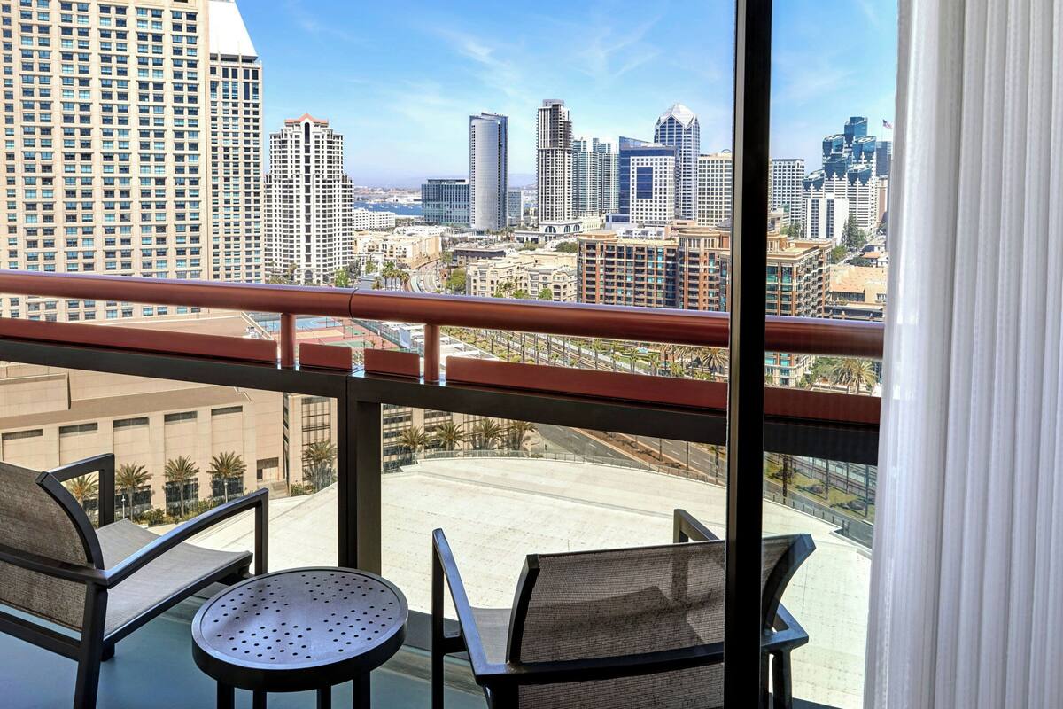 A balcony with two chairs and a table, overlooking a cityscape with high-rise buildings.