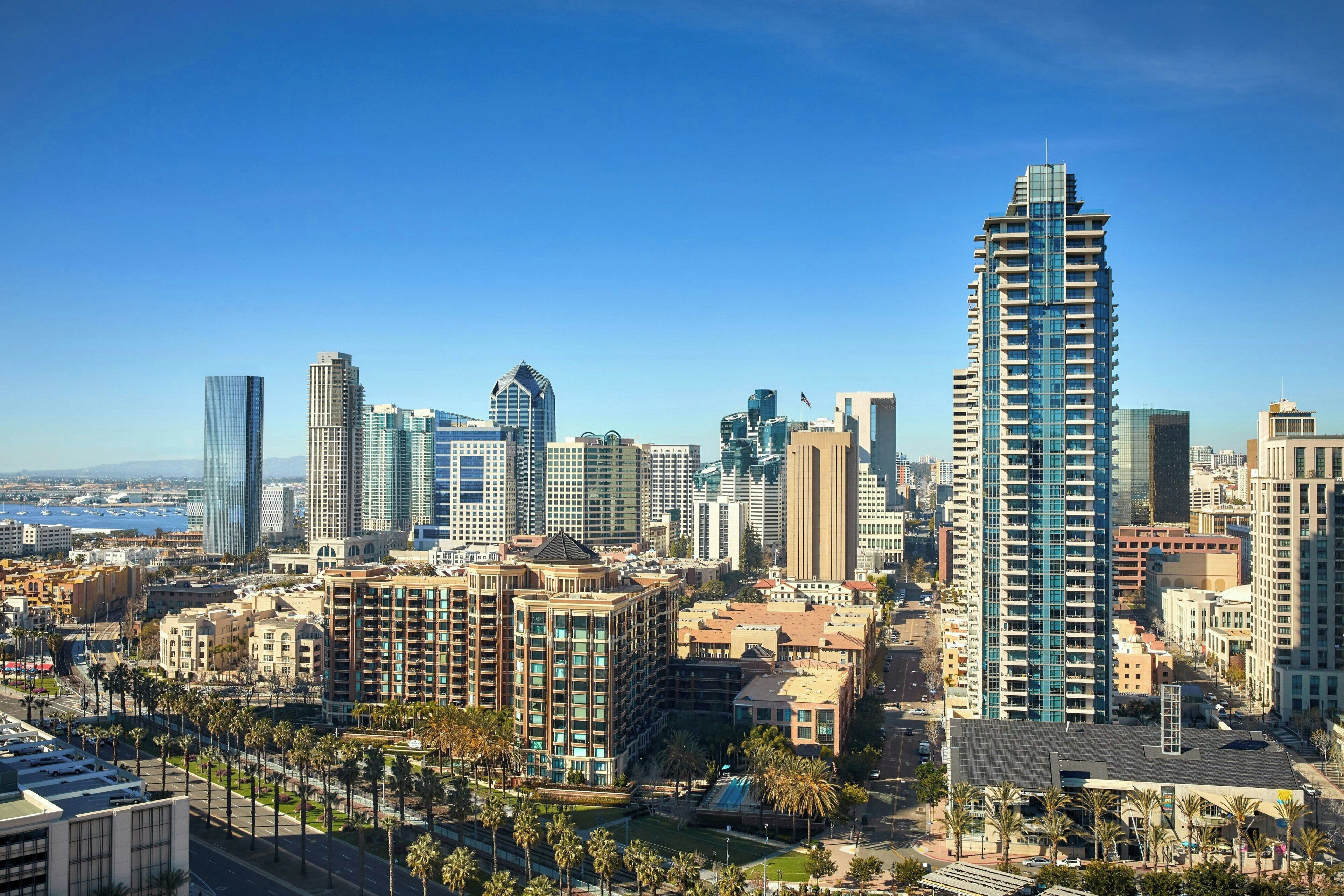 Bybillede med høje bygninger, palmer og en klar himmel.