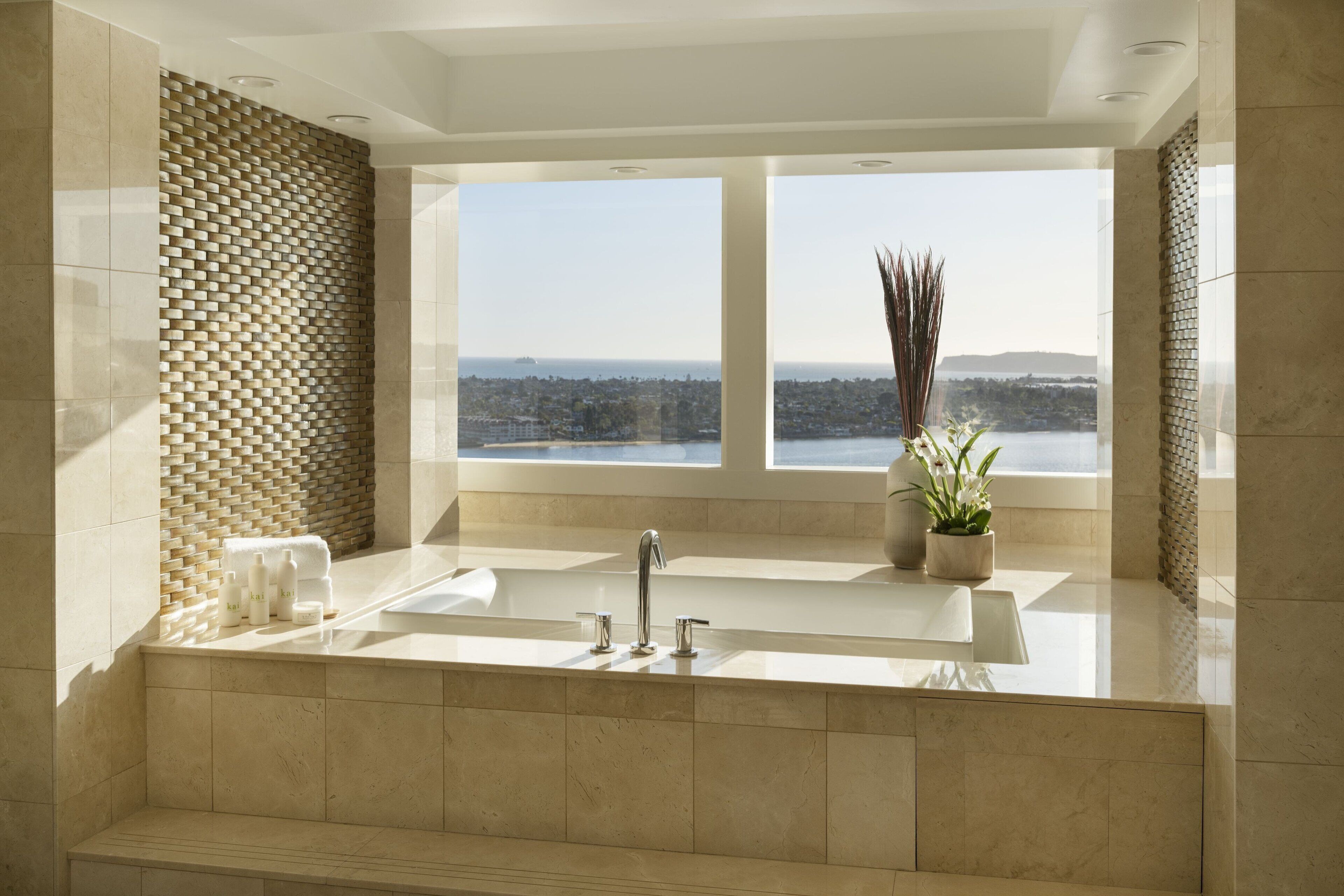 A modern bathroom with a large bathtub, a sink, and a window offering a city view.
