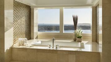 A modern bathroom with a large bathtub, a sink, and a window offering a city view.