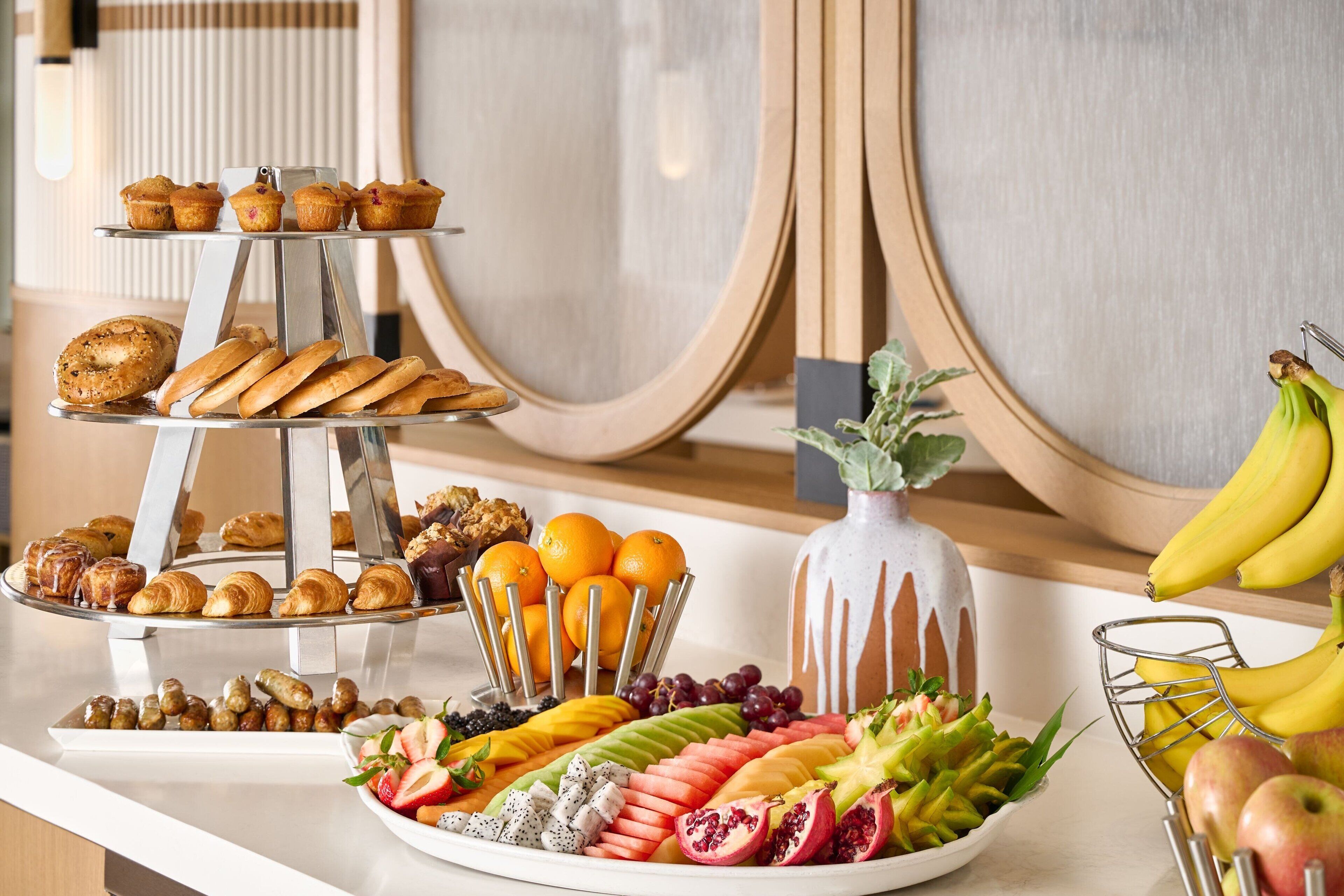 Buffet de l'esmorzar amb pastissos, fruites i un ram de flors decoratiu.