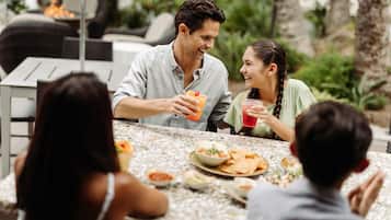 Un grupo de personas cenando al aire libre en una mesa con diversos platos y bebidas.