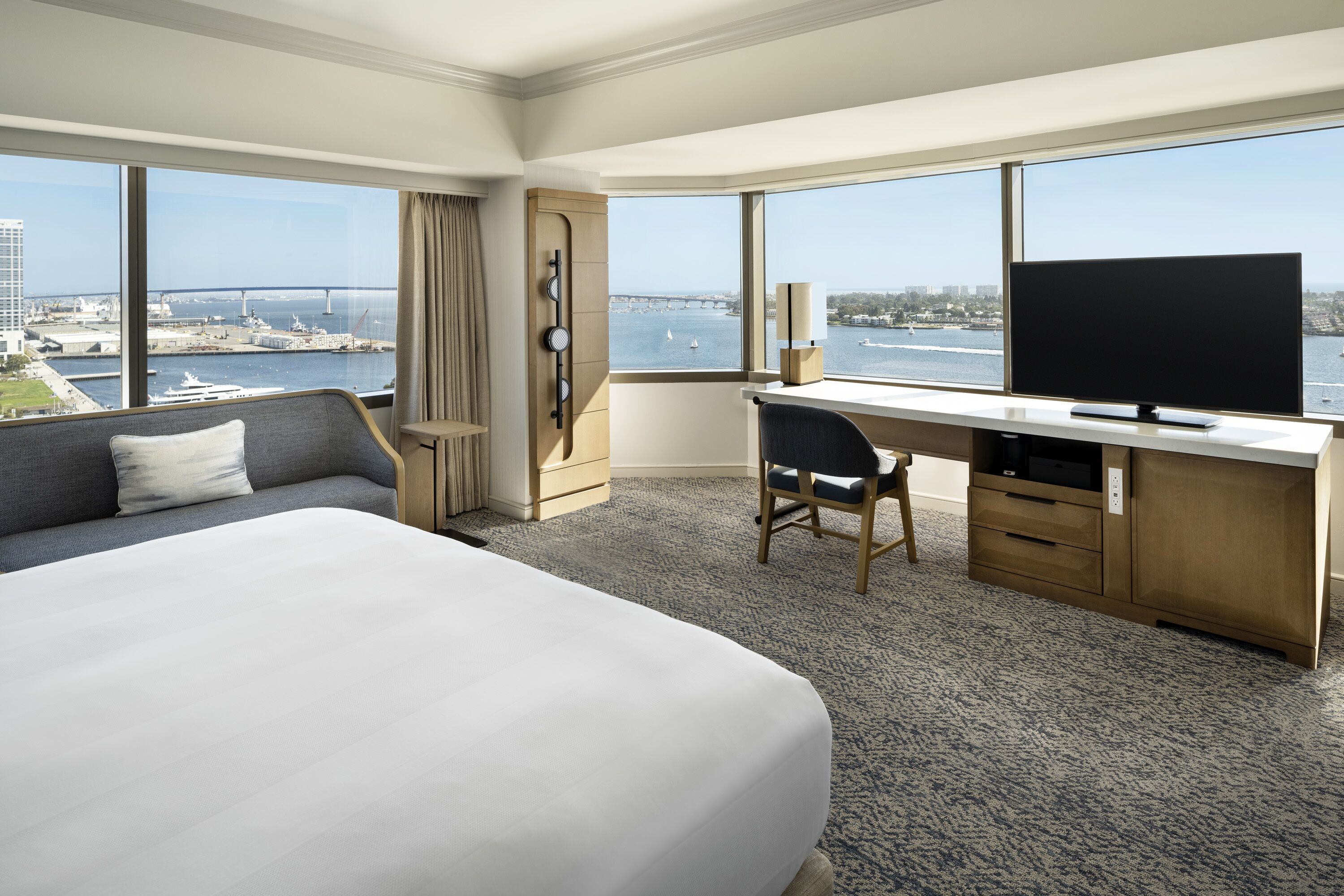 Habitación de hotel con una cama grande, un escritorio con silla, televisión y vista al agua y al puente.
