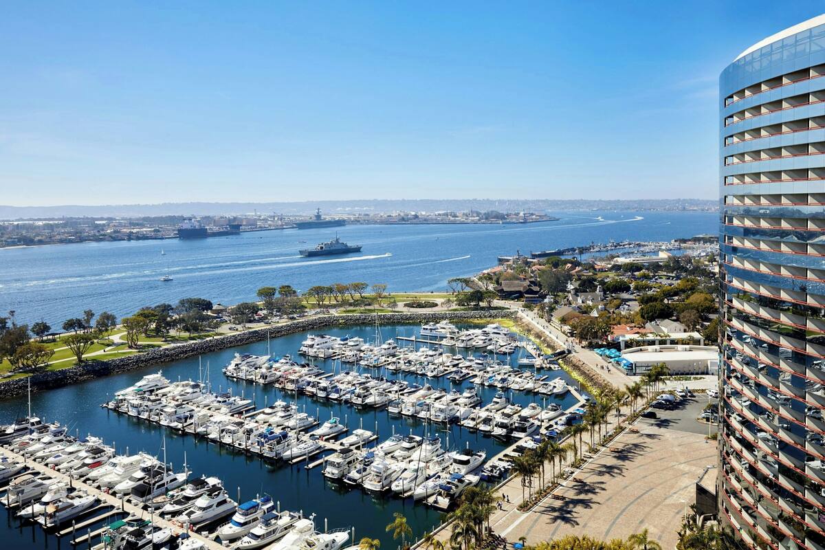 A marina with numerous boats docked, a large ship in the background, and a modern building with balconies.