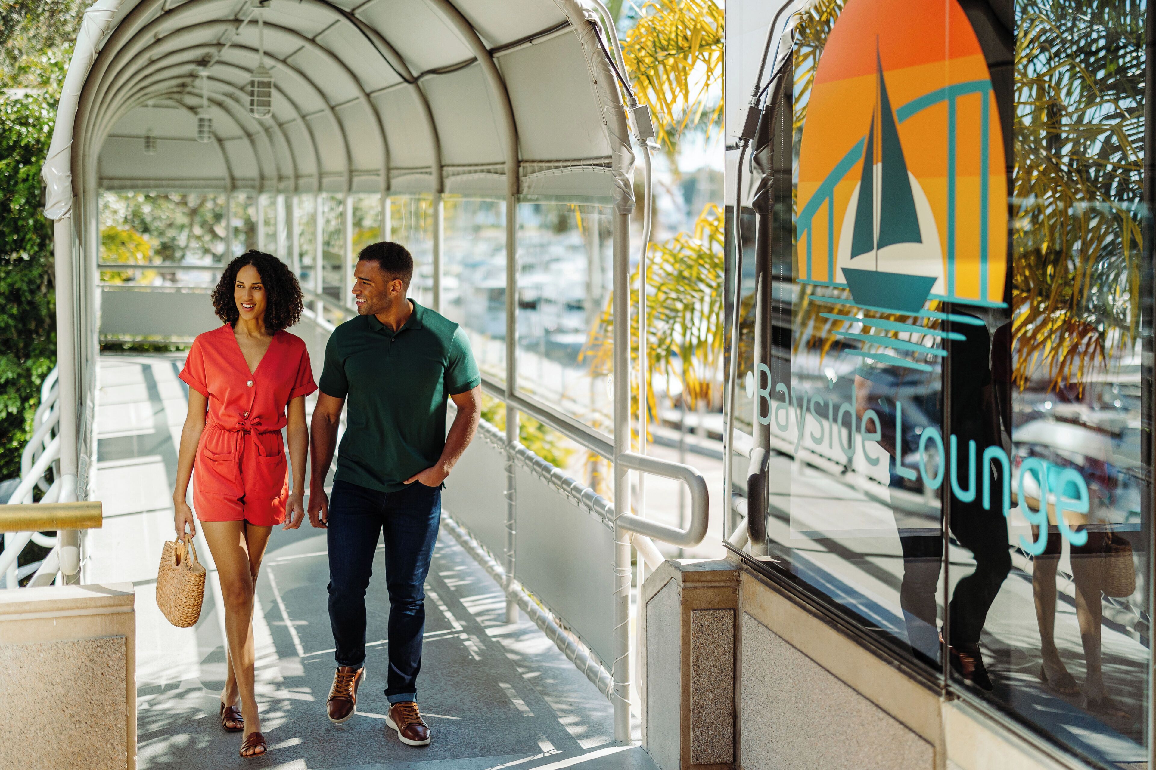 A covered walkway with a glass door leading to a building with a logo that reads "By the Sea Lounge."