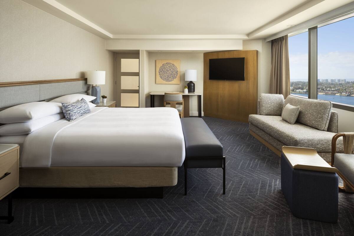 A hotel room with a large bed, a sofa, a desk, and a TV.