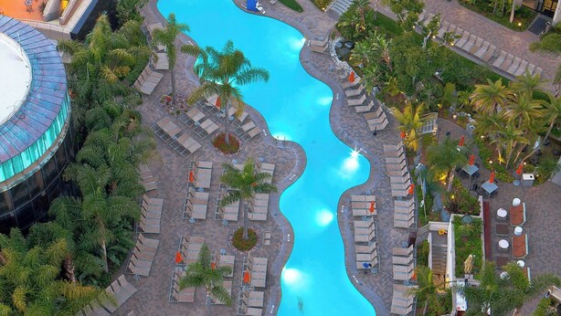 Vista aérea de un complejo turístico con varias piscinas, zonas de descanso y palmeras.