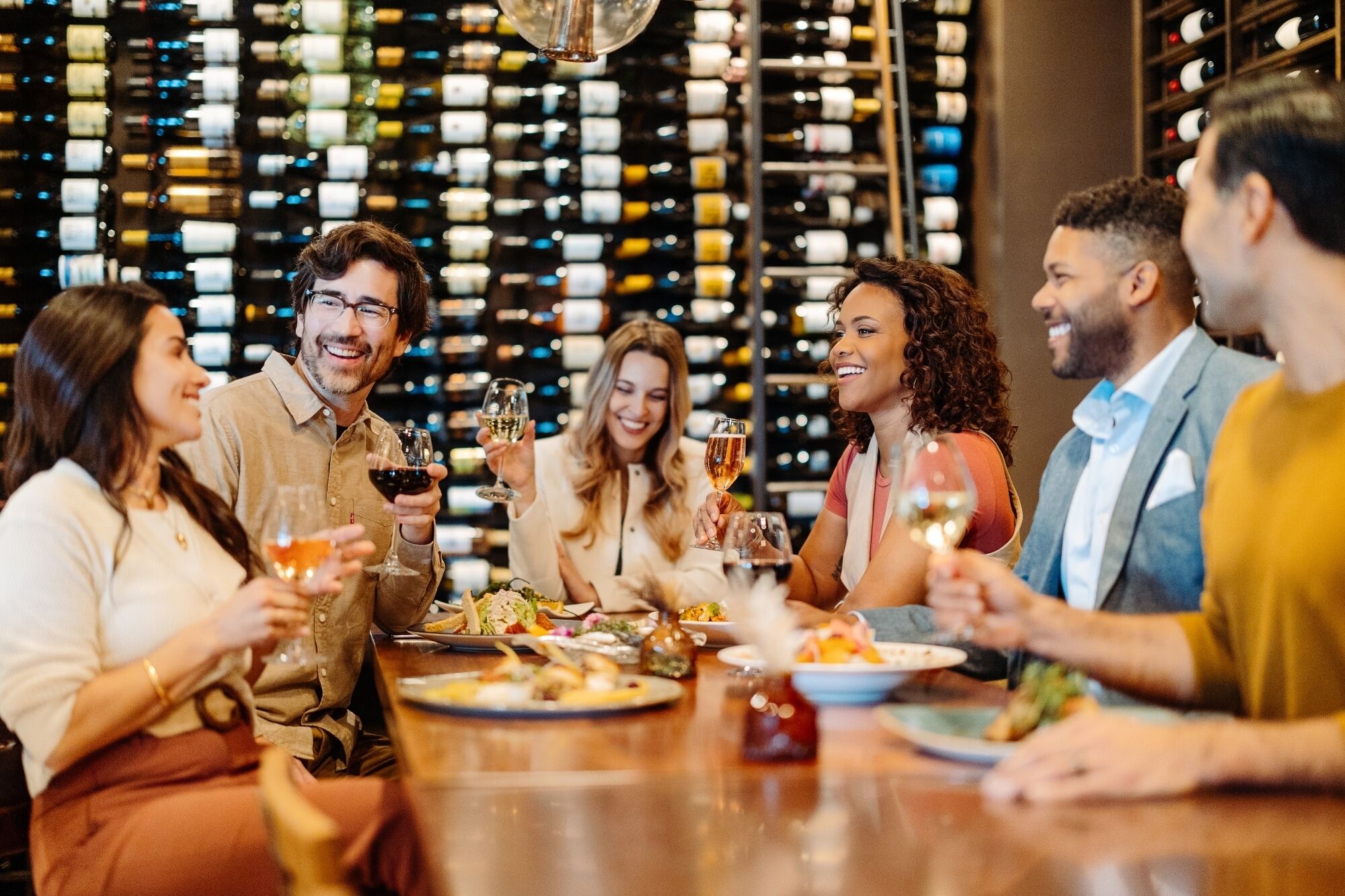 A group of people dining at a restaurant with a wine rack in the background.