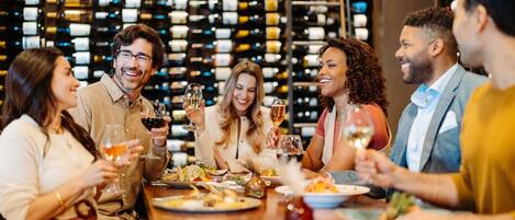 A group of people dining at a restaurant with a wine rack in the background.