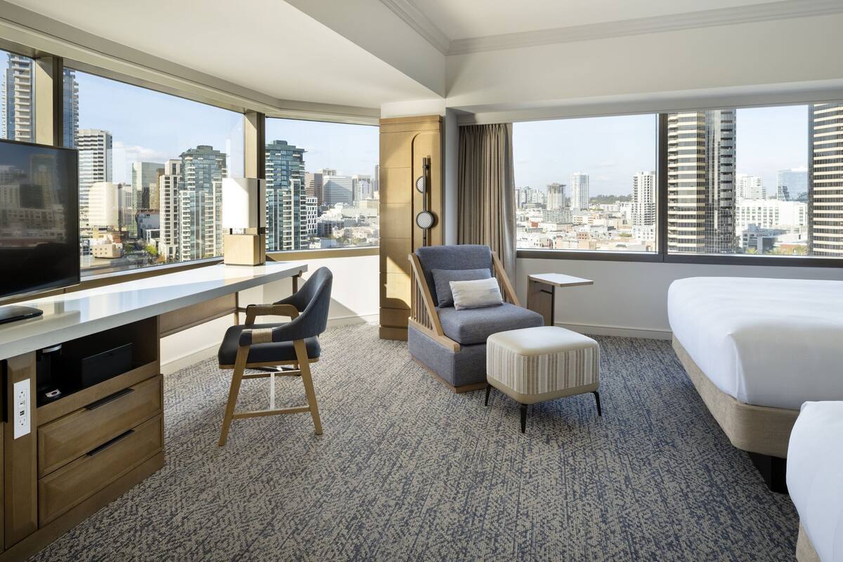 A hotel room with a city view, a desk with a chair, a sofa, a bed, and a small table.