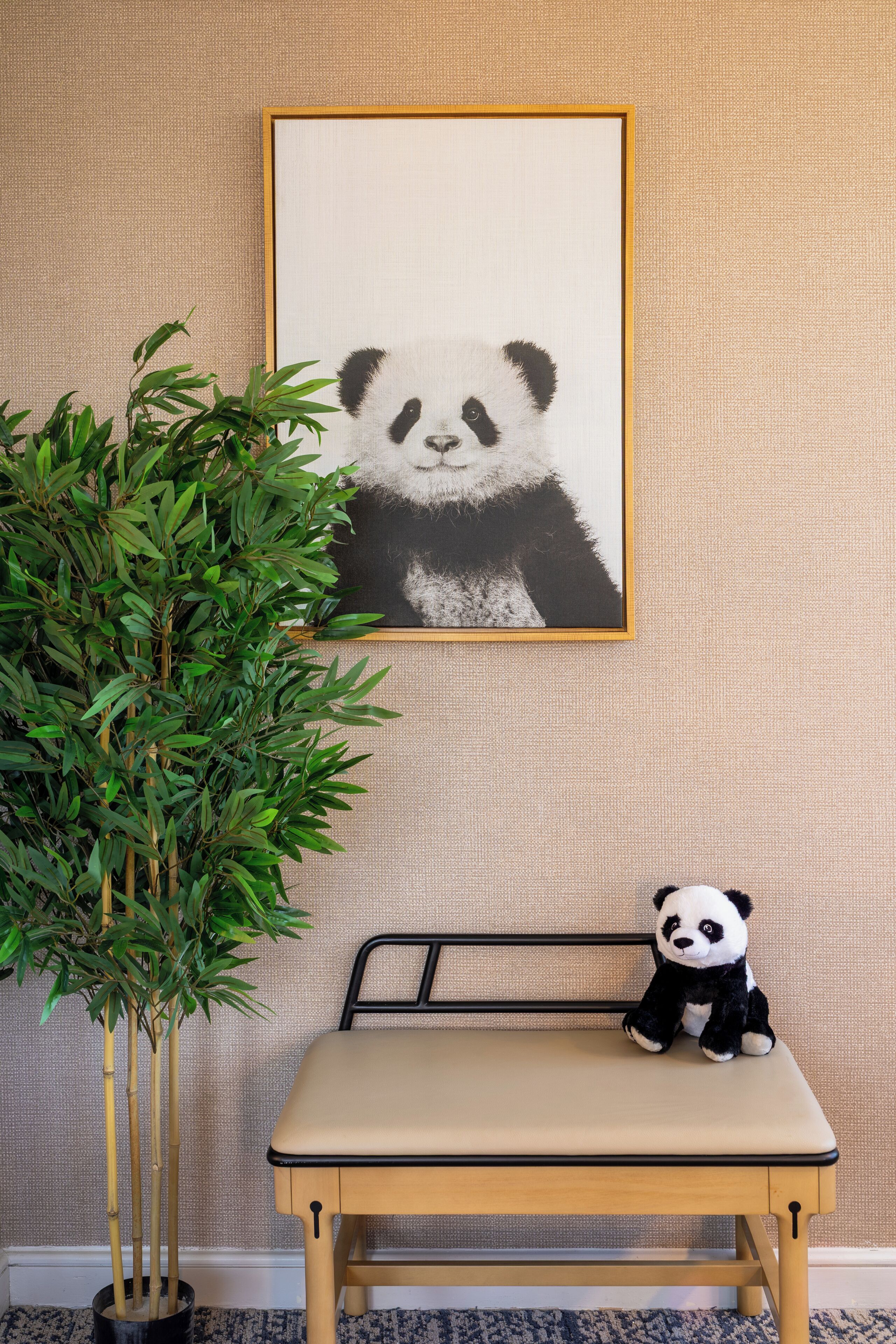 A room with a framed panda artwork on the wall, a bamboo plant, and a small table with a panda plush toy.