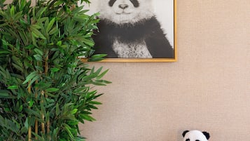 A room with a framed panda artwork on the wall, a bamboo plant, and a small table with a panda plush toy.