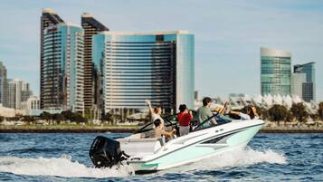A speedboat with passengers on a body of water, with a city skyline in the background.