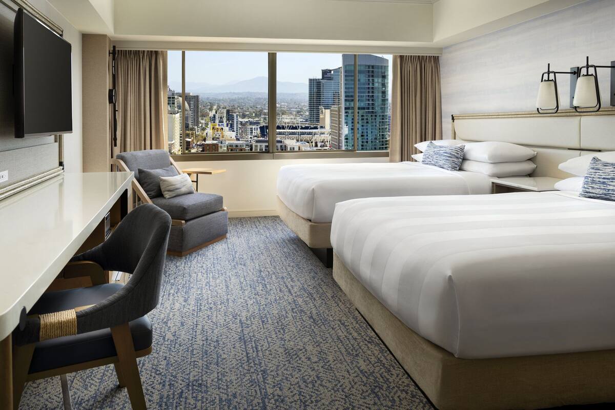 A hotel room with two beds, a desk, a chair, and a TV.