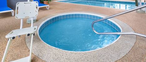 An indoor swimming pool with a circular edge, a pool lift, blue lounge chairs, and a potted plant.