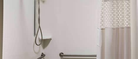 A bathroom with white tiled walls, a shower with a handheld showerhead, and a toilet with a grab bar.