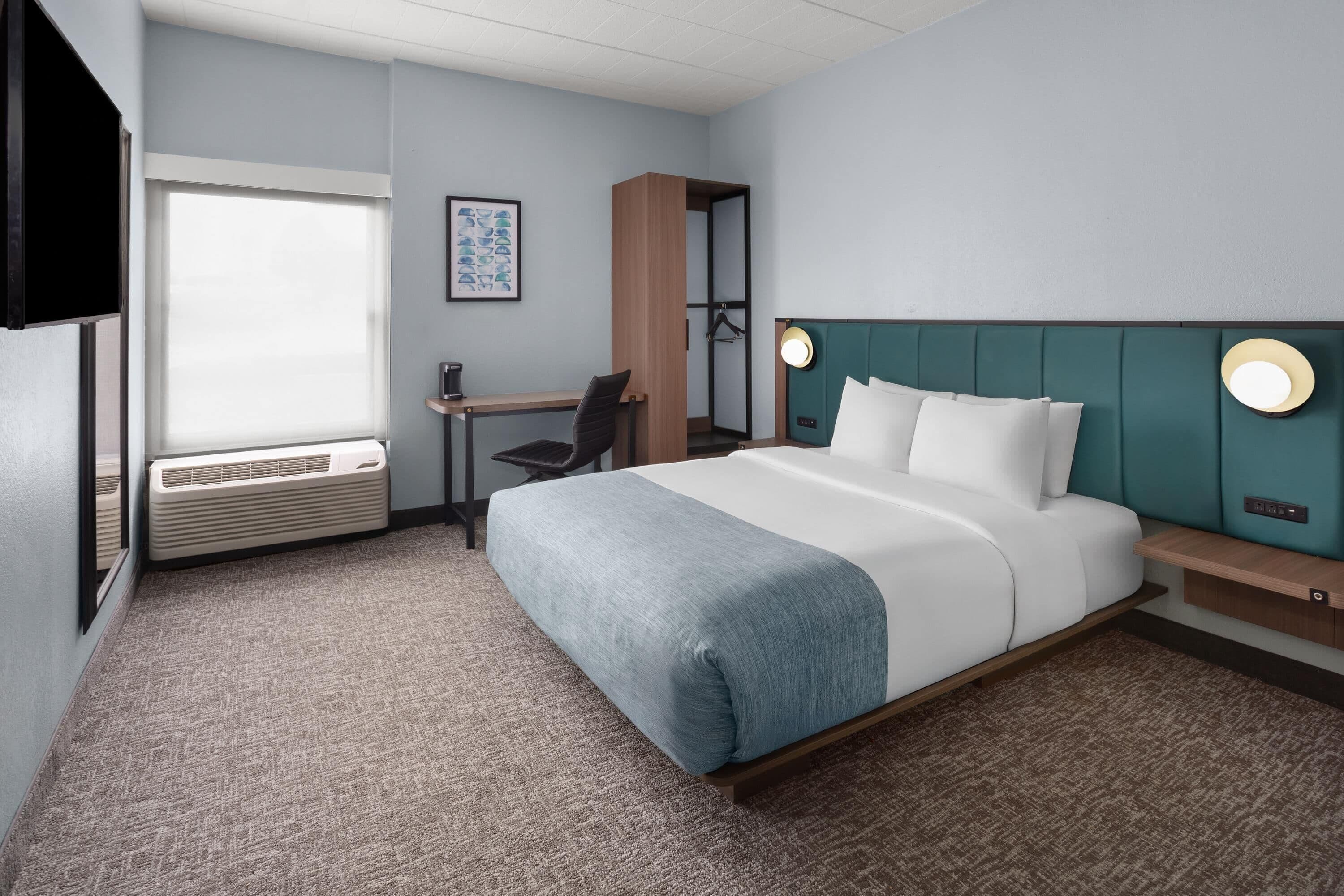 Ein Hotelzimmer mit Bett, Schreibtisch, Stuhl und einem großen Fenster.