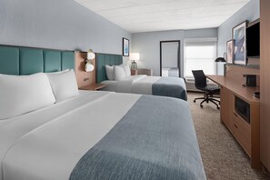 A hotel room with two beds, a desk, a chair, a TV, and a large window.