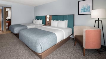 Habitación de hotel con dos camas, un escritorio, una silla, una lámpara y un cuadro en la pared.