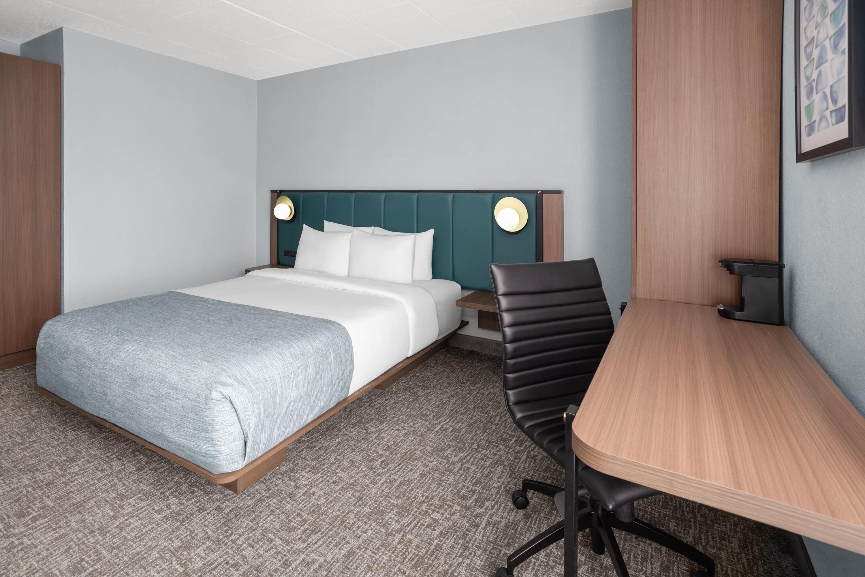 A hotel room with a bed, a desk, a chair, and a nightstand.