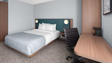 A hotel room with a bed, a desk, a chair, and a nightstand.