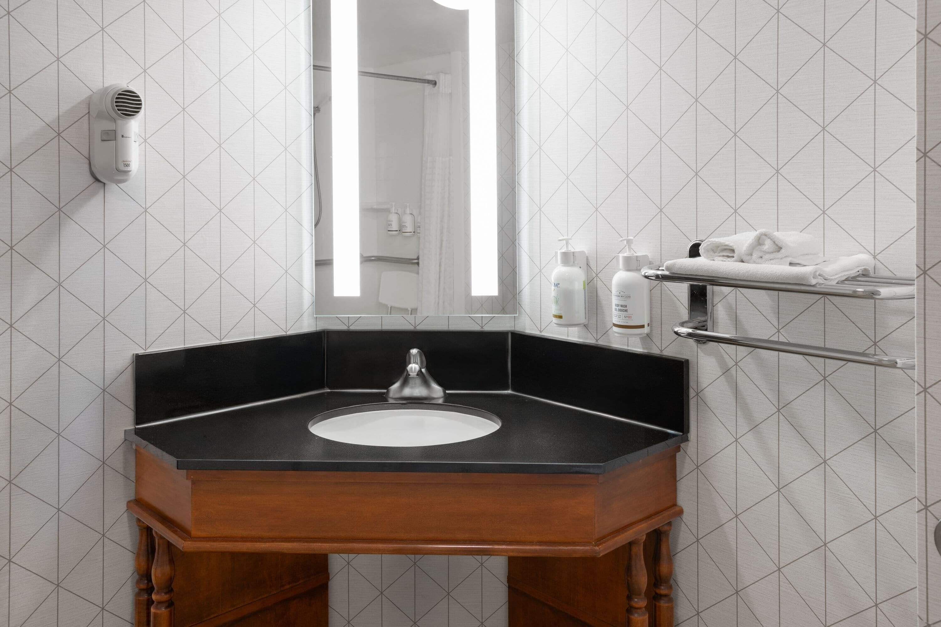 A bathroom with a black countertop sink, a mirror, a towel rack, and a hair dryer mounted on the wall.