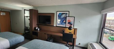 A hotel room with two beds, a desk, a television, and artwork on the wall.