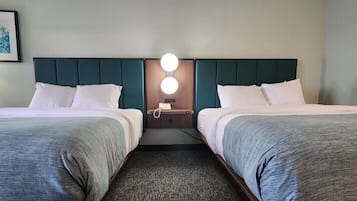 Camera d'albergo con due letti, un comodino con una lampada e un faretto a parete.