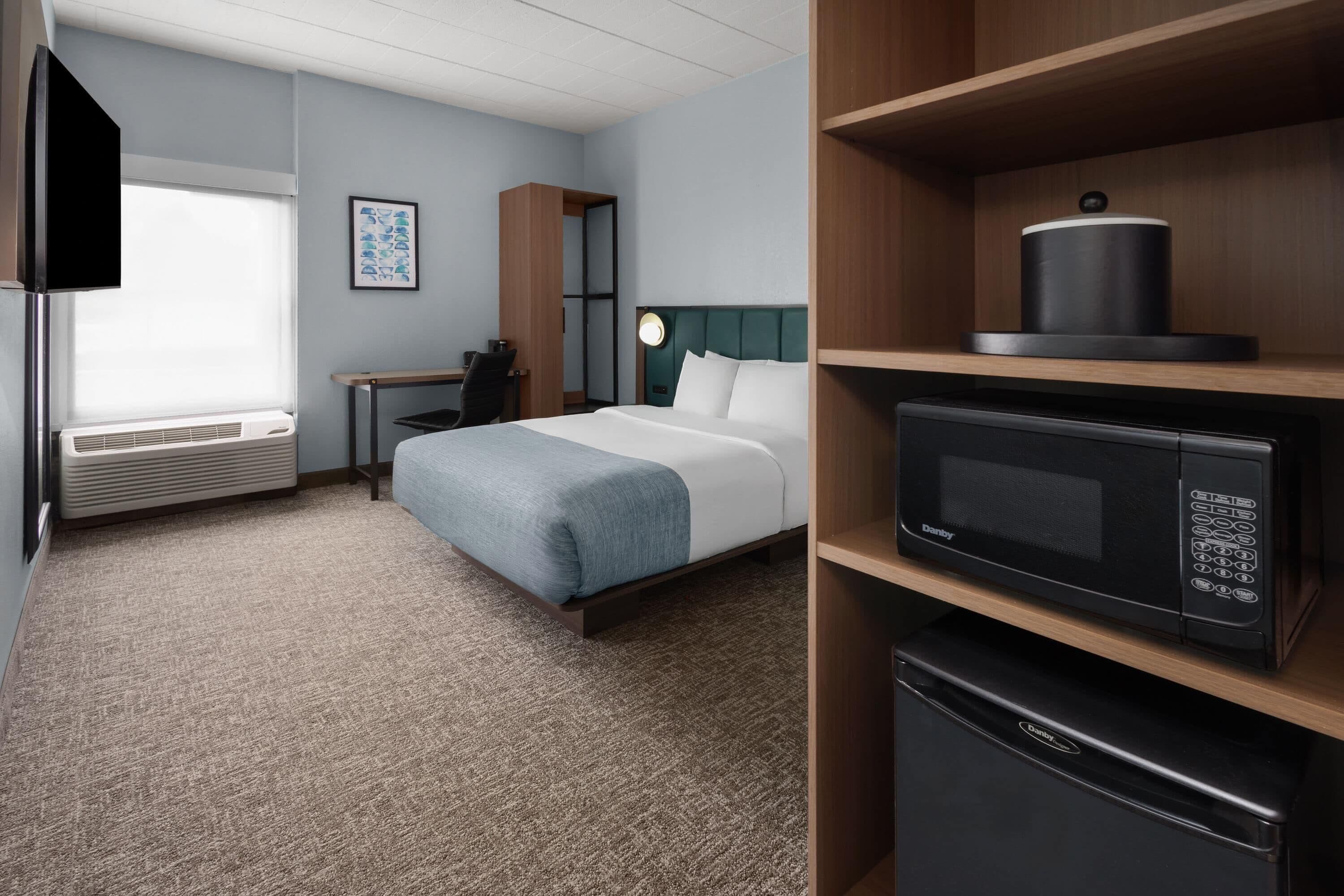 A hotel room with a bed, a desk, a flat-screen TV, a microwave, and a refrigerator.