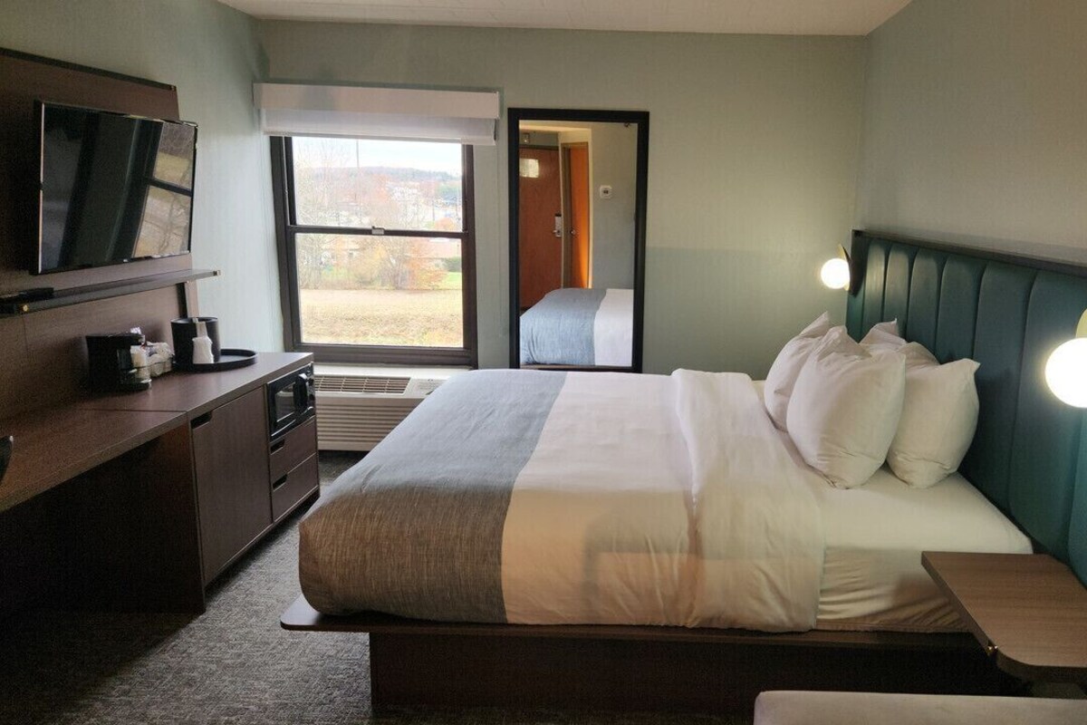 A hotel room with a bed, bedside table, TV, and a view of the outdoors.