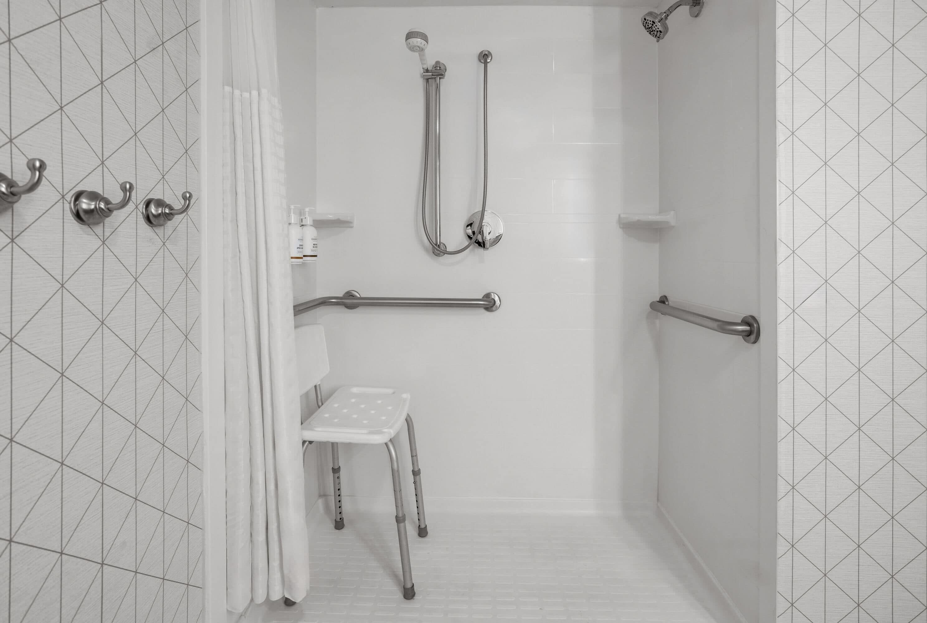 A shower area with grab bars, a shower chair, and a handheld showerhead.