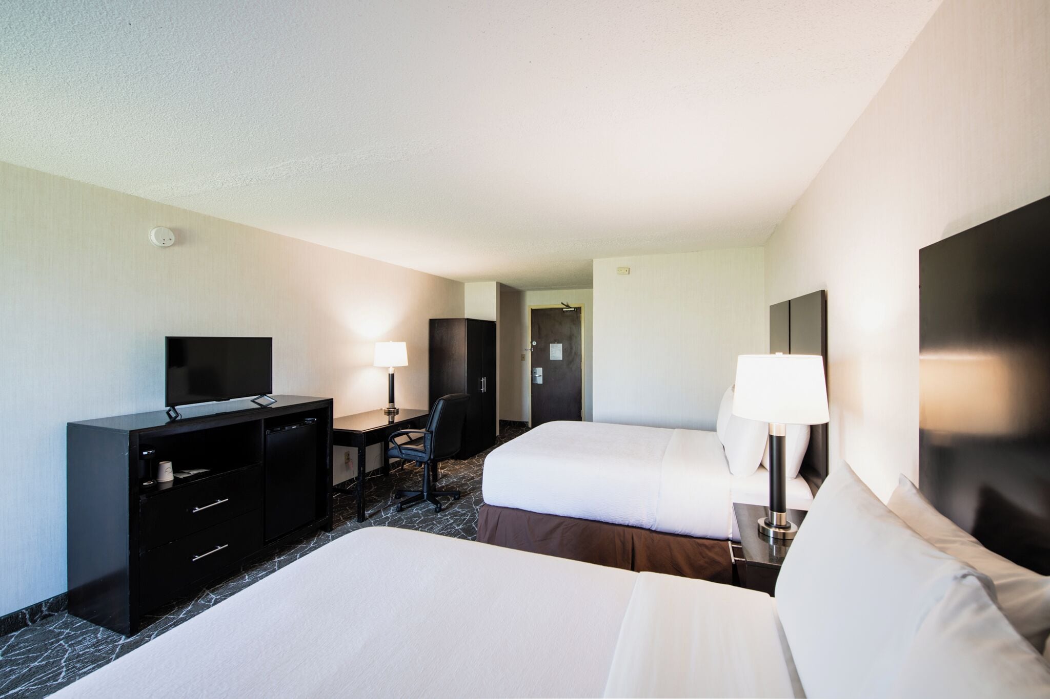 A hotel room with two beds, a desk with a chair, a television, and a lamp.