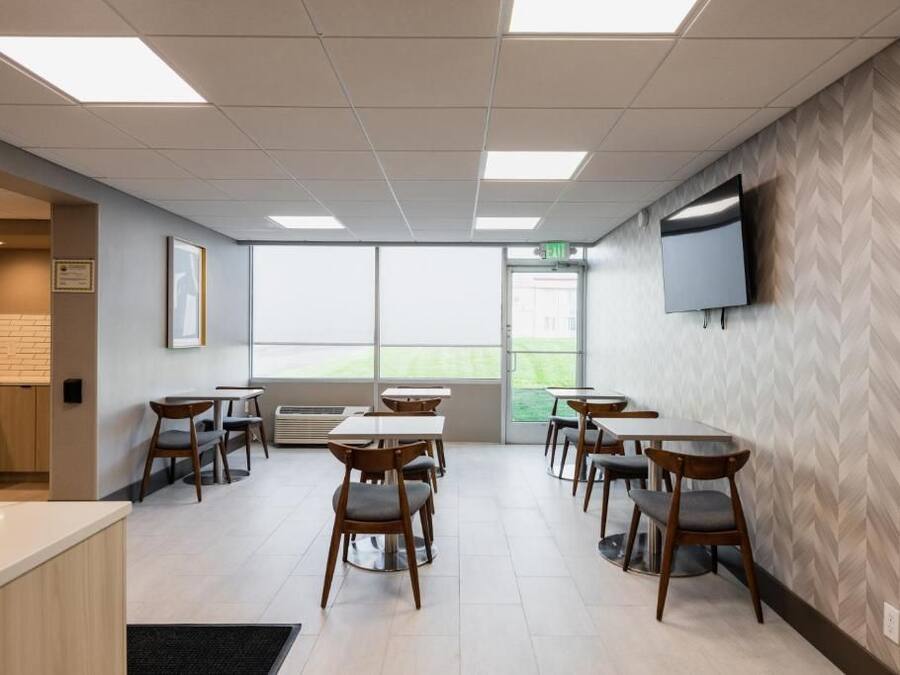 A modern dining area with tables and chairs, a flat-screen TV on the wall, and a large window providing natural light.