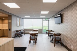 Un comedor moderno con mesas y sillas, un televisor de pantalla plana en la pared y un amplio ventanal que proporciona luz natural.