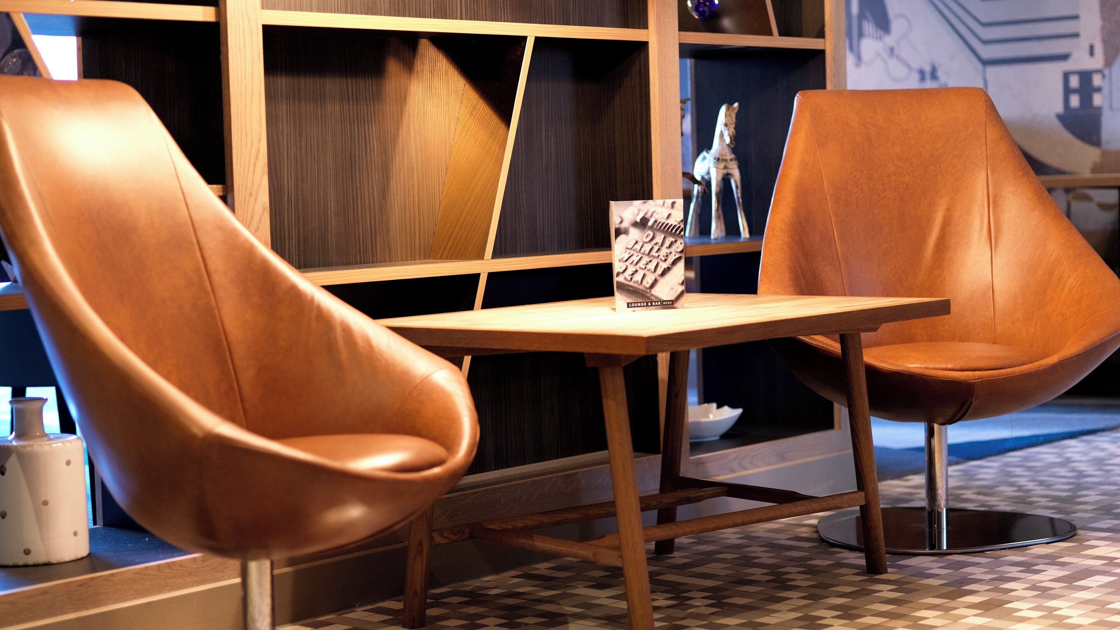 A seating area with two leather chairs and a table, a menu stand, and a patterned floor.