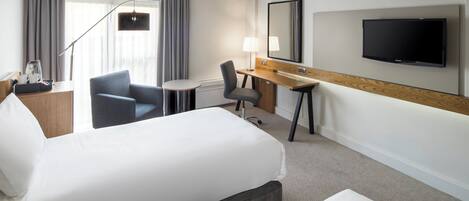 A hotel room with two beds, a desk, a chair, a TV, and a window with curtains.