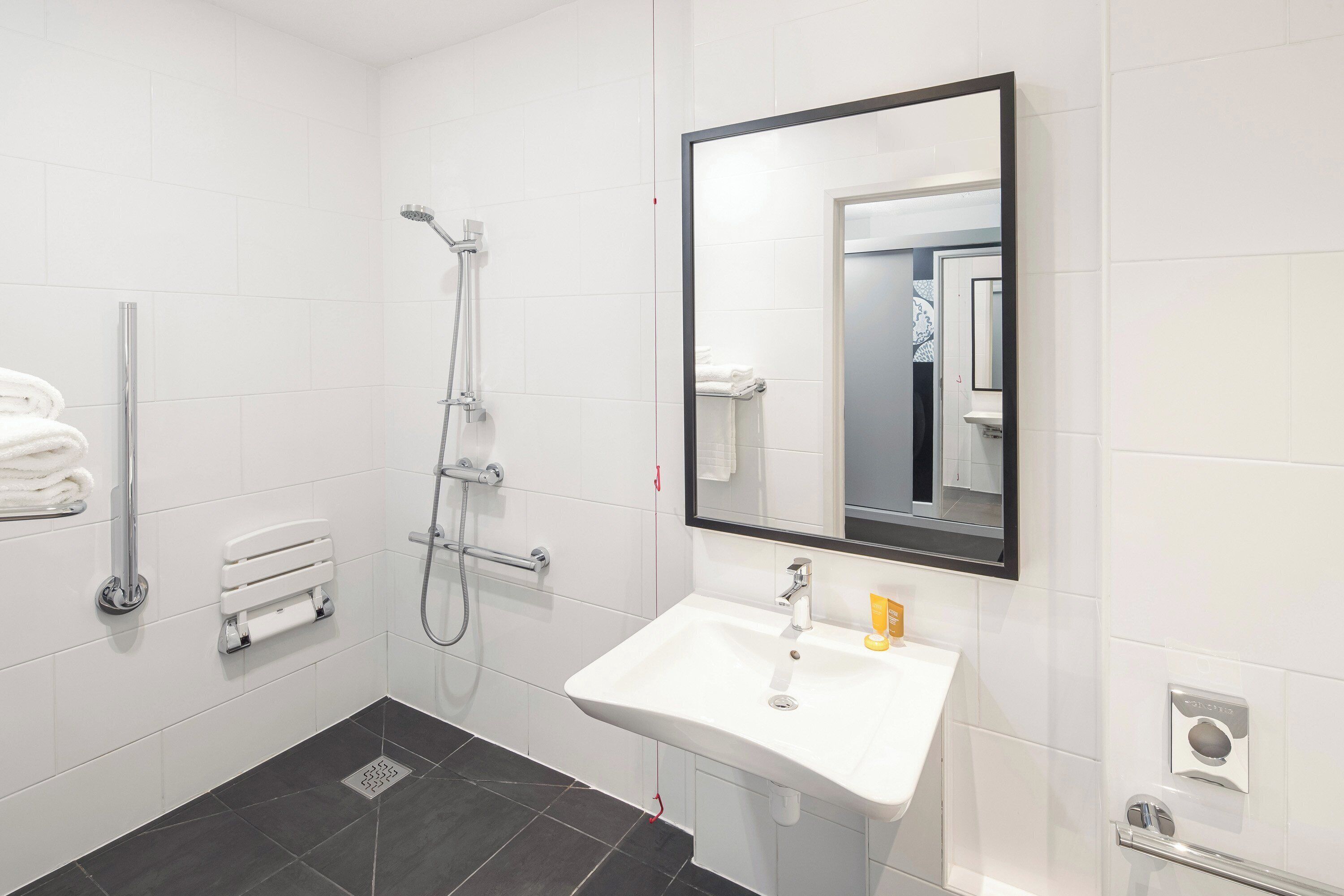 A modern bathroom with a white sink, a large mirror, a shower with a handheld showerhead, and a towel rack.