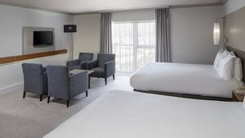 Ett hotellrum med en stor säng, två fåtöljer, en platt-TV som är monterad på väggen och ett stort fönster med gardiner.