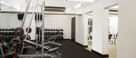 A gym with weightlifting equipment, dumbbells, and a mirror.