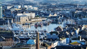 A harbor with numerous boats, a prominent chimney, and a mix of residential and commercial buildings.
