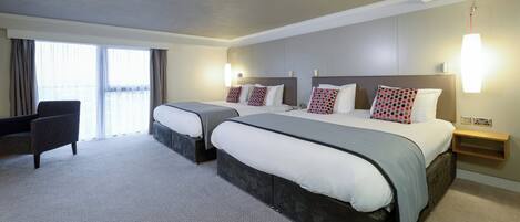 Une chambre d’hôtel avec deux lits, une chaise, un bureau et une grande fenêtre.