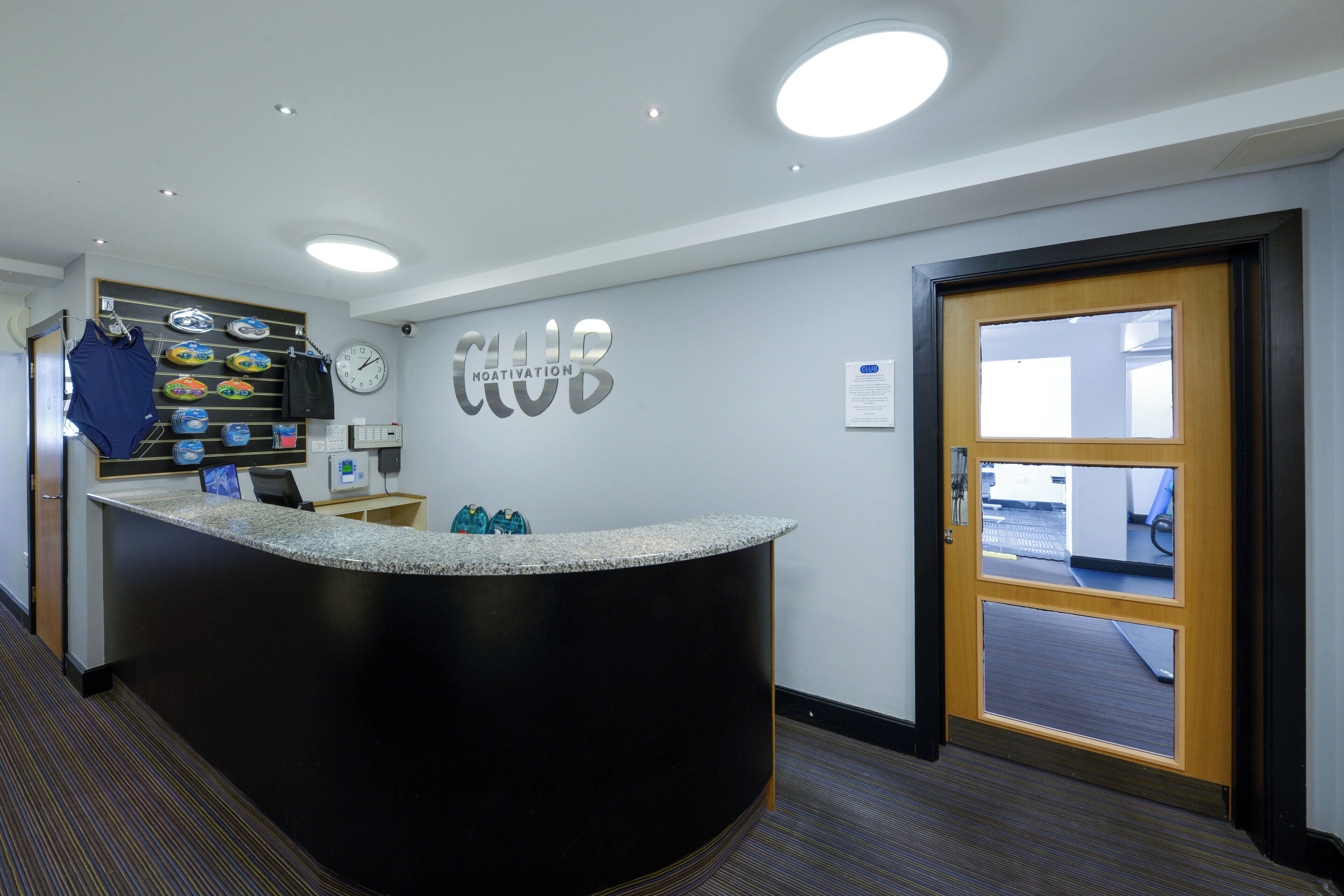 A reception area with a counter, a clock, and a door leading to a gym.