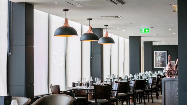 A restaurant with long tables, dark chairs, and pendant lighting.